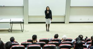 Female speaker addressing an audience in a university lecture hall, representing an academic setting related to Cox MBA Scholarships.
