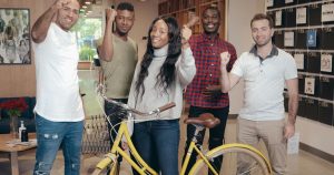 A diverse group of young professionals posing with a yellow bicycle, celebrating their journey with the Dream Together Master's Scholarship.