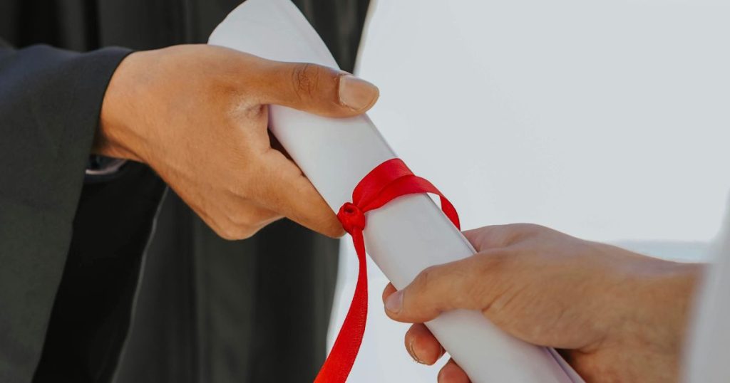 Close-up of a graduate receiving a certificate tied with a red ribbon, symbolizing academic achievement and opportunities like the EBS Scholarship.